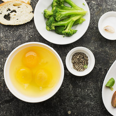 Ingredients for cooking scrambled eggs or omelets with green herbs, fresh vegetables, broccoli and turmeric as a healthy breakfast or lunch option. View from above. Against a ldark background
