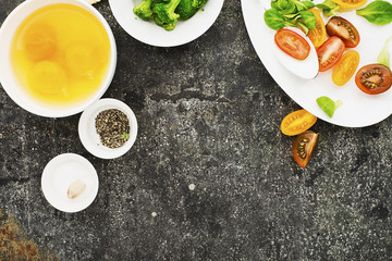 Ingredients for cooking scrambled eggs or omelets with green herbs, fresh vegetables, broccoli and turmeric as a healthy breakfast or lunch option. View from above. Against a ldark background
