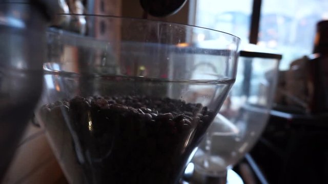 Barista scooping coffee beans and dropping them into coffee grinder.