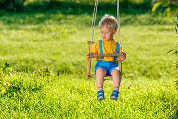 Rural scene with toddler boy swinging outdoors.