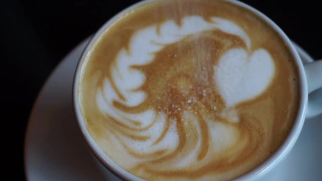 White sugar falling over cappuccino milk foam and dissolving 
