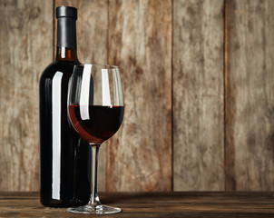 Bottle and glass with red wine on wooden table