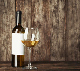 Glass of white wine and bottle with blank label on wooden table. Mock up for design