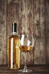 Bottle and glass with white wine on wooden table