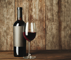 Glass of red wine and bottle with blank label on wooden table. Mock up for design
