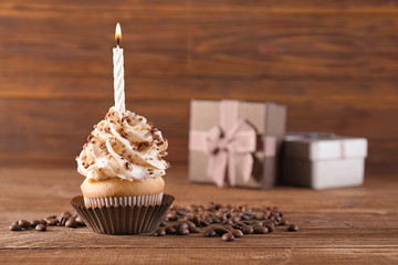 Birthday cupcake with candle on table against wooden background