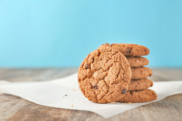 Delicious oatmeal cookies with chocolate chips on wooden table against color background