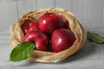Paper bag with ripe red apples on table