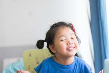 Happy funny Little asian girl eating yogurt and she holding spoon in her hands.