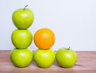 Many apples and an orange on the wooden table.