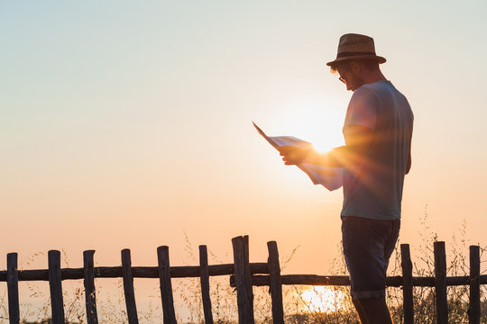 Young hipster man exploring map over the sunset at seaside