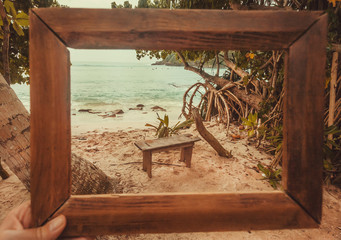 Photoframe for the memory about ocean tropical beach. Wooden banch under palm trees on warm waves bay