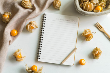 Cape gooseberry fruit and notepad on white wooden background