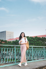 Fototapeta na wymiar Full length of asian girl walking on a bridge with city view with a book in her hand