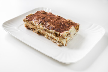 Plate with slice of homemade tiramisu, on white background. Main ingredients: ladyfingers, cream with mascarpone, cocoa powder, coffee, eggs