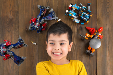 The boy lies on a floor, he is surrounded a toy by designers robots and soldiers
