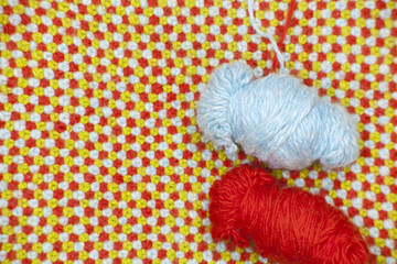 Клубок красной и голубой пряжи на фоне из вязанного полотна с красной, голубой и зеленой шерсти