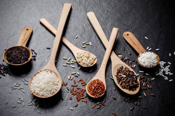 Mixed rice, White rice, Jasmine rice, Black rice, Brown rice, Riceberry and Raw rice in wooden spoon over black desk background
