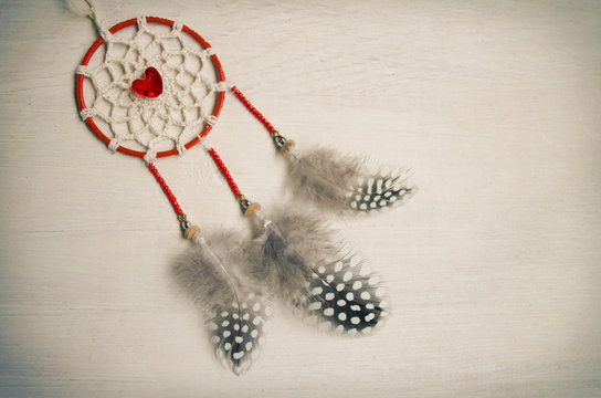 Dreamcatcher with feathers on a wooden background. Ethnic design, boho style, tribal symbol.Red heart as a symbol of Valentine's day
