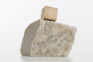 Minimalist composition with small wooden cube on top of a block of marble rock