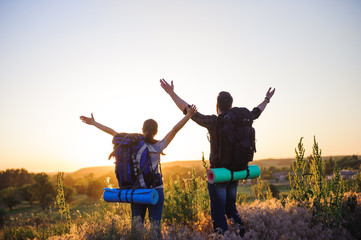 Silhouettes of two hikers with backpacks walking at sunset. Trekking and enjoying the sunset view