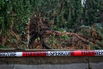 Entwurzelter Baum unscharf im Hintergrund Absperrband der Feuerwehr scharf im Vordergrund