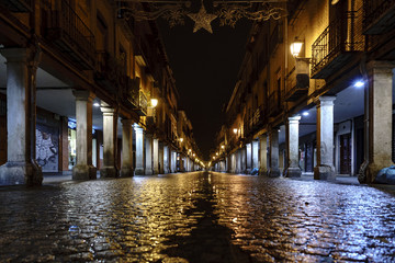 low-angle shooting of the main street of Alcala de Henares (Spain) called "Mayor" on a cold and rainy night with wet cobblestones and with light reflections