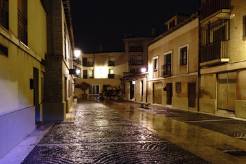 Plaza called Corral de la Sinagoga in Alcala de Henares (Spain) on a cold and rainy night with wet paving stones and light reflections