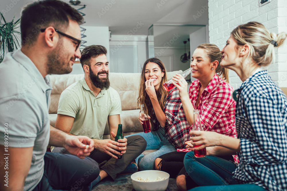 Wall mural group of happy young friends having fun and drinking beer in home interior