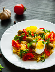 fusilli pasta salad with tomato, eggs and olive in plate on dark wooden background