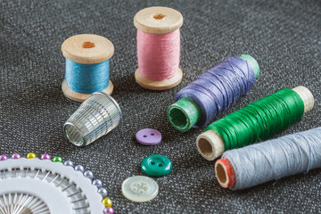 Sewing accessories: spools of threads, needles, thimble, buttons on the textured fabric surface