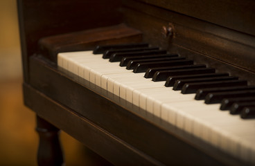 Fototapeta na wymiar Close up of piano keys and old vintage wooden upright piano, shallow focus, warm brown tone