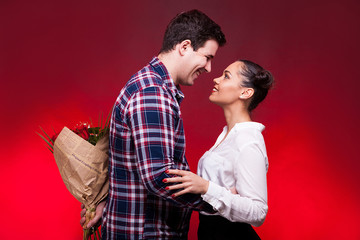 Man with a roses bouquet at his back on a first date. Red background and studio photo