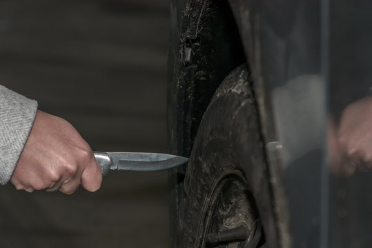 A Woman Holds A Knife In Her Hand And Wants To Sting With It In A Car Tire. Slashing Into A Car Tire. Concept: Vandalism And Crime