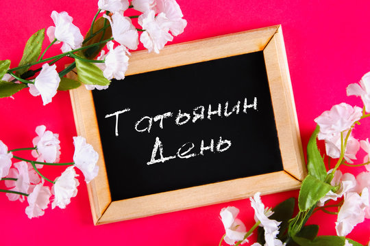 The inscription in Russian: Tatyanin day. Russian holiday on student's day. A chalk plaque surrounded by white flowers on a pink background.