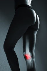 Human knee joint and leg in x-ray, on gray background. The knee joint is highlighted by red colour.