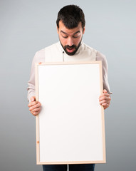 Handsome man with vest holding an empty placard on grey background