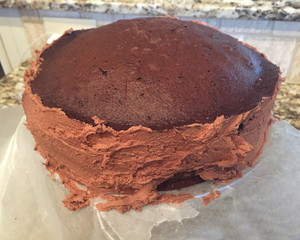 Homemade chocolate cake being frosted with buttercream frosting.