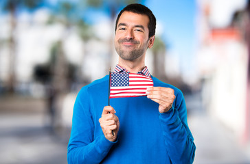 Handsome young man holding an american flag on unfocused background