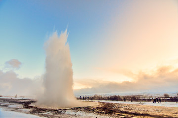 Strokkur geysir wowing the small group of tourists who surround it as it explodes out of the ground at dawn.