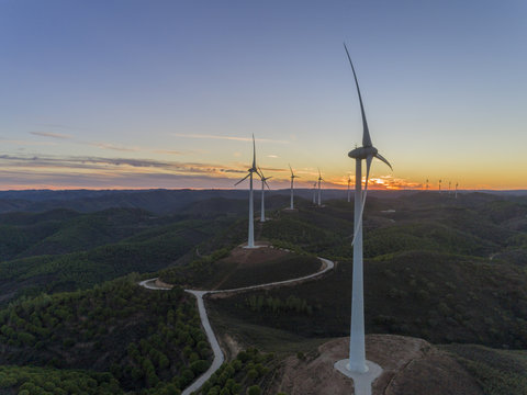 Aerial panoramic Wind farm turbines silhouette at sunset. Clean renewable energy power generating windmills. Algarve countryside.