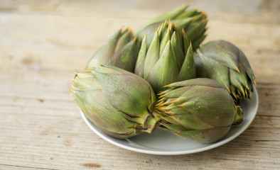 Five artichokes on the white plate on the wooden table