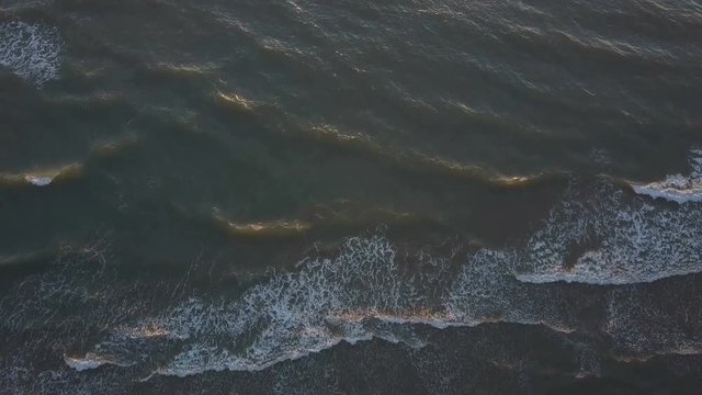 Aerial view of waves crashing on the beach as sunset