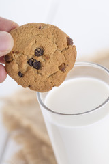 A chocolate cookie being dunked in a glass of milk.

