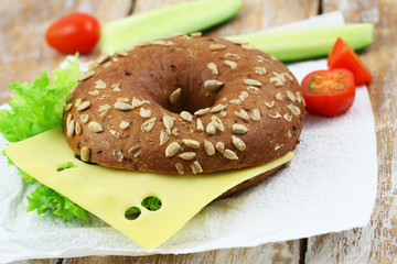 Brown bagel with sunflower seeds with cheese and lettuce, closeup
