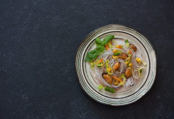 Rice noodles with seafood and vegetables over black stone background. Top view
