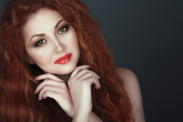 Fototapeta premium Close up portrait of a gorgeous smiling red headed woman with beautiful make up, her hands crossed under her chin. Isolated on grey background. Copy-space
