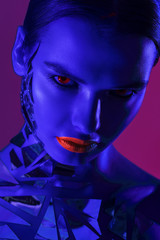 Close up vertical portrait of a girl in a high fashion, beauty style with blue skin, red lips make up at dark background. Devil makeup fashion art design. Halloween holiday concept