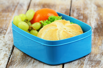 Packed lunch containing cheese roll, grapes and mandarine in blue lunch box
