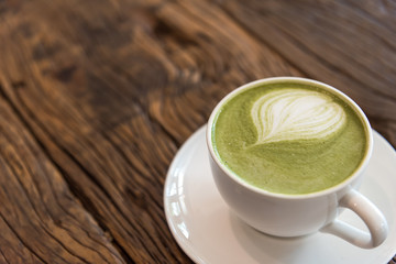 Selected focus on a hot green tea latte art decorated on wooden background. Hot matcha green tea mixed with milk foam art decorated on surface.